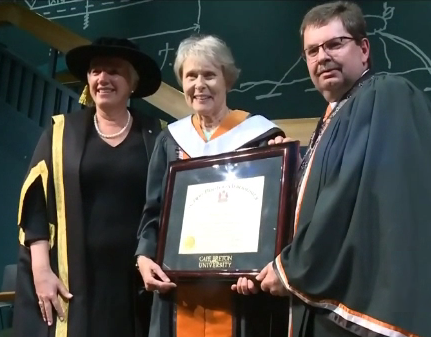 Image of Roberta Bondar with award and two people in graduation gowns